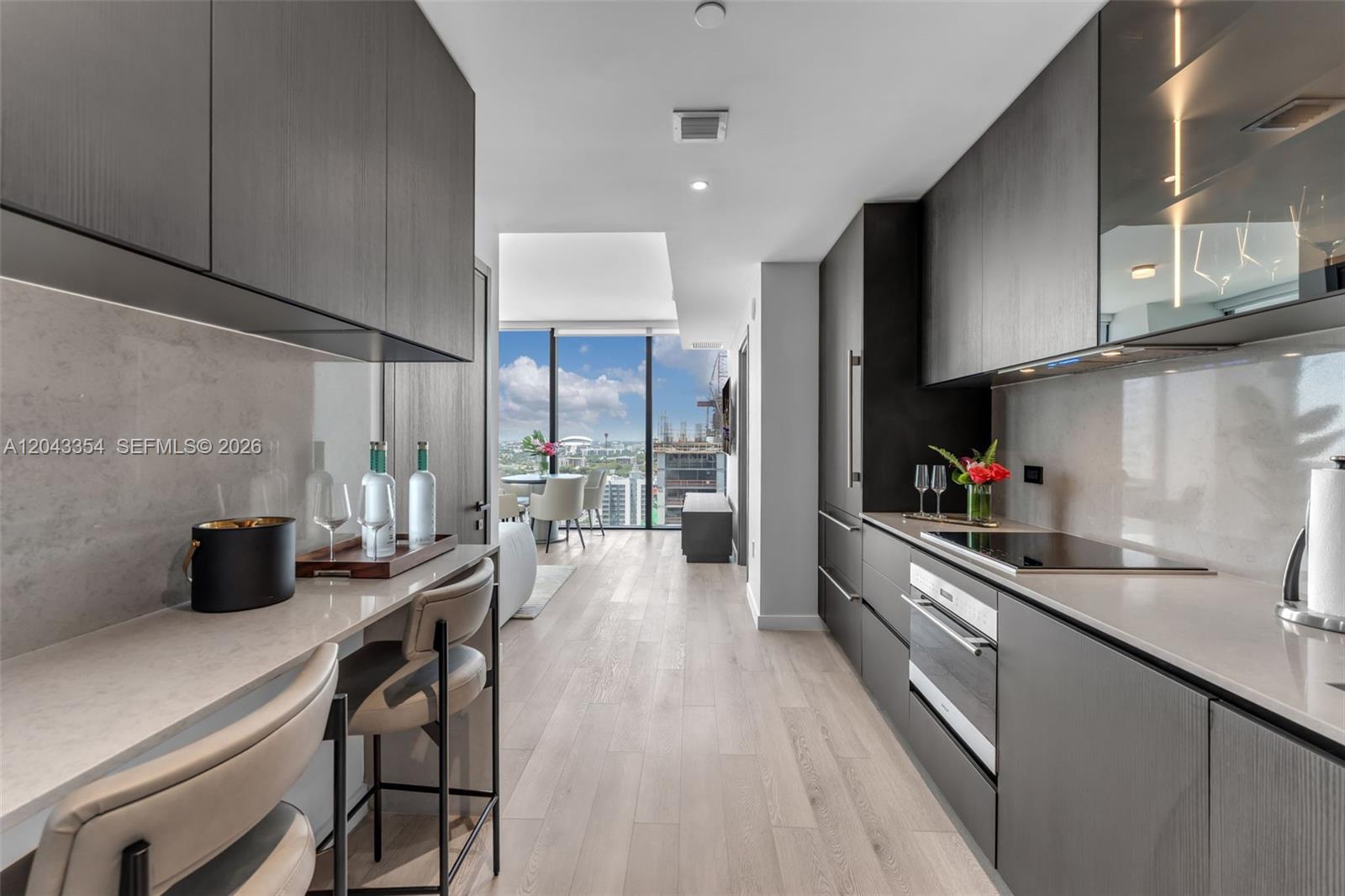 A modern galley kitchen features dark wood cabinetry, light stone countertops, and floor-to-ceiling windows — 20 NE 11th Street # 3410, Miami FL 33132, MIAMI, FL