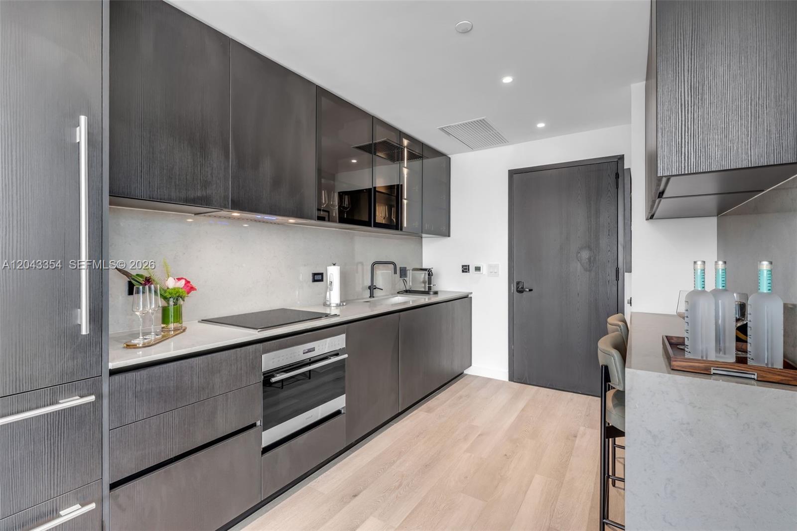 A modern kitchen features dark wood cabinetry, light stone countertops, and light wood flooring — 20 NE 11th Street # 3410, Miami FL 33132, MIAMI, FL