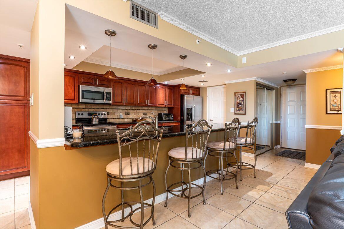 A kitchen with dark wood cabinets, granite countertops, and three bar stools at the island — 1915 Lavers Circle # E309, Delray Beach FL 33444, DELRAY BEACH, FL
