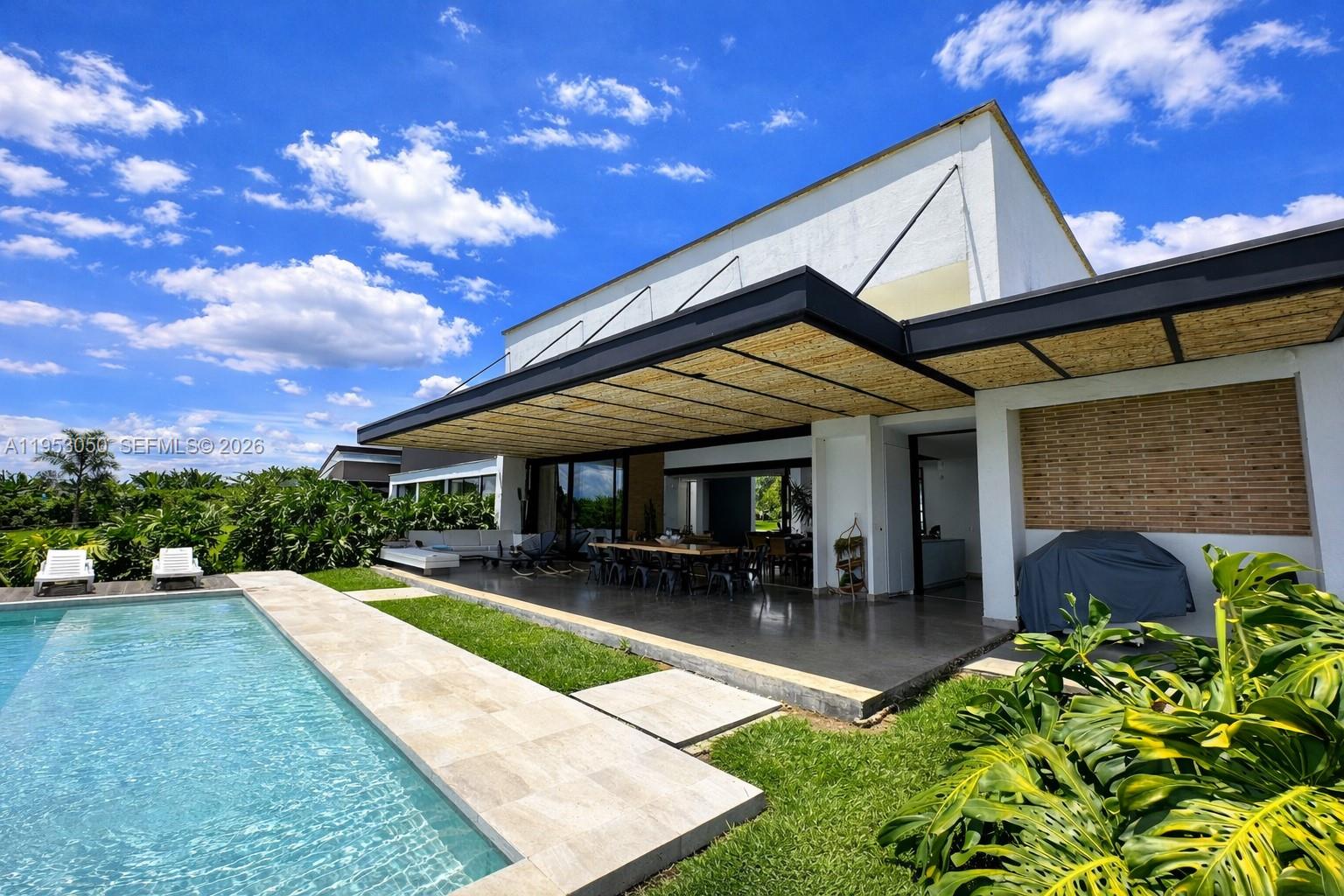 A modern house exterior features a covered patio, swimming pool, and lush green landscaping — Finca La Pradera Montenegro Quindio Colombia, FL