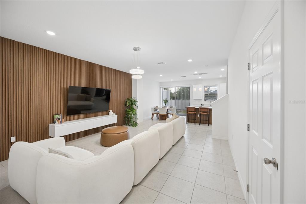 A modern living room features a slatted wood accent wall, white sofa, and open kitchen — 1220 WYCLIFFE WAY, ST CLOUD, FL