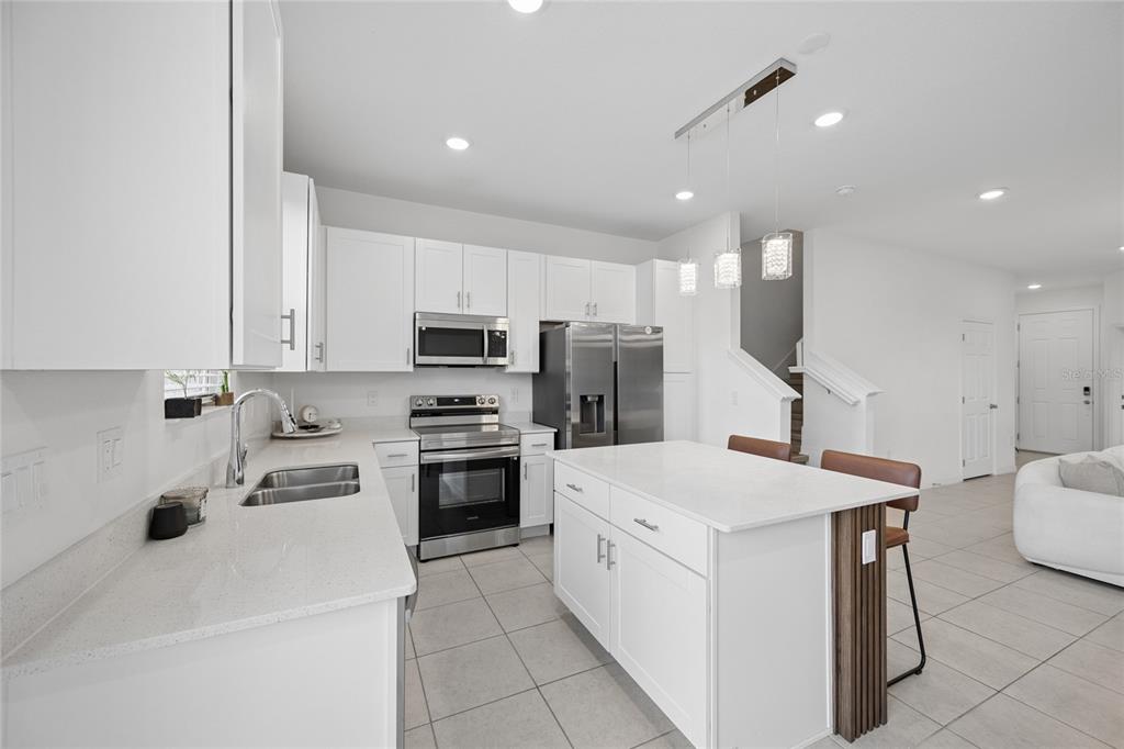 A modern kitchen features white cabinets, stainless steel appliances, a quartz island, and tile flooring — 1220 WYCLIFFE WAY, ST CLOUD, FL