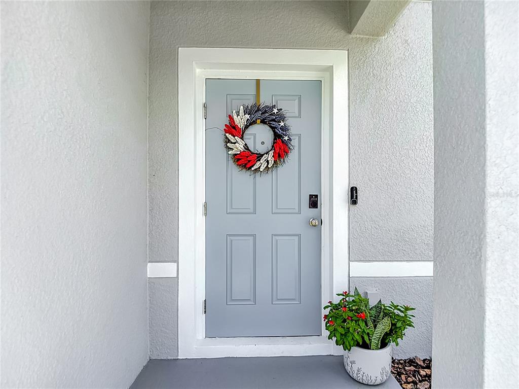 A light blue front door with a patriotic wreath sits under a covered entryway — 12000 GRIZZLY LANE, NEW PORT RICHEY, FL