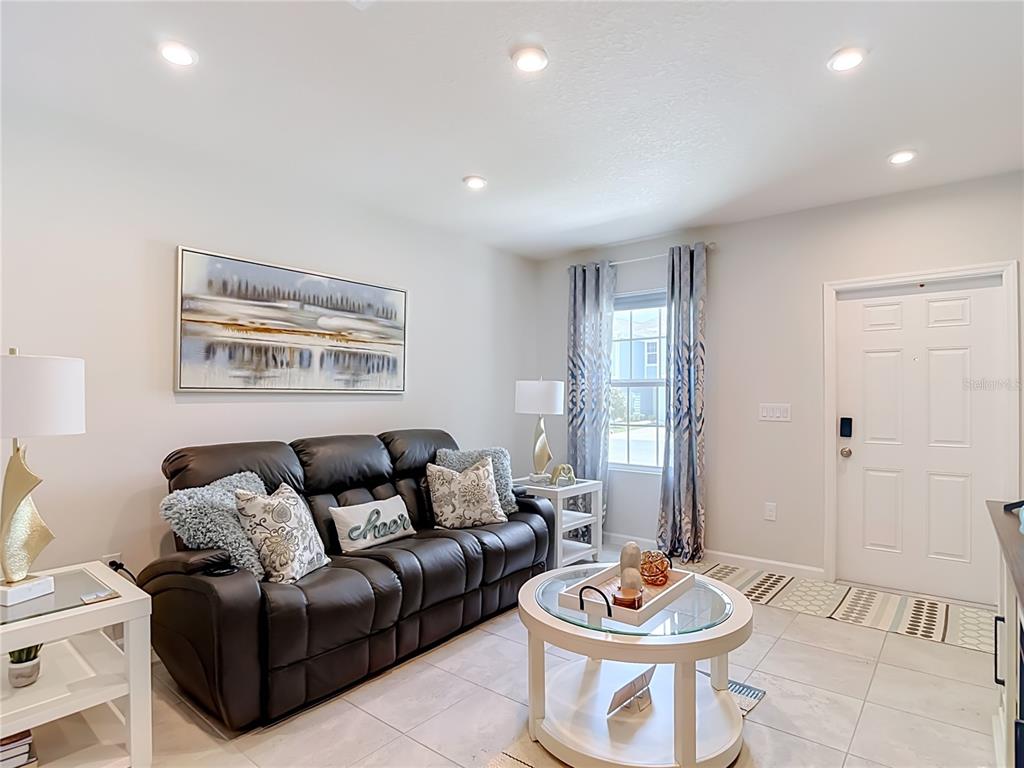A living room features a dark leather sofa, a round glass coffee table, and tile flooring — 12000 GRIZZLY LANE, NEW PORT RICHEY, FL