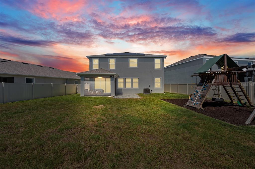 The backyard of a two-story house features a screened-in patio and a wooden playset — 8693 BOWER BASS CIRCLE, WESLEY CHAPEL, FL