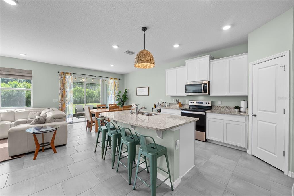 A kitchen with white cabinets, granite countertops, and a central island with green metal stools — 8693 BOWER BASS CIRCLE, WESLEY CHAPEL, FL
