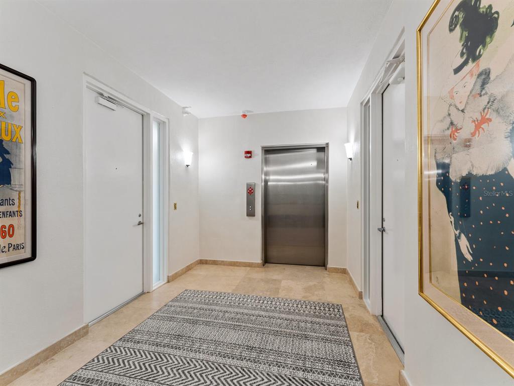 A hallway features a stainless steel elevator, white doors, tiled floors, and framed wall art — 1511 GULF OF MEXICO DRIVE UNIT 201, LONGBOAT KEY, FL