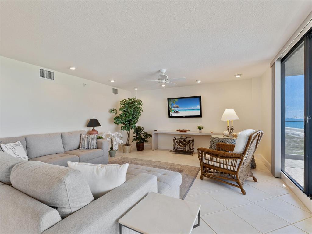 A living room features a gray sectional sofa, wicker chair, and a view of the ocean — 1511 GULF OF MEXICO DRIVE UNIT 201, LONGBOAT KEY, FL