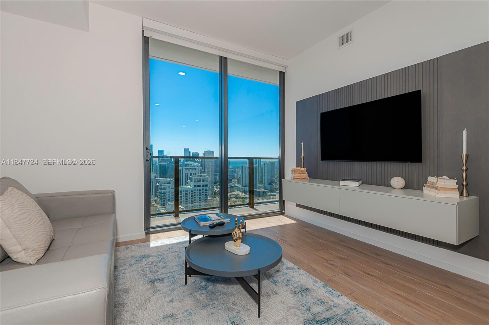 A modern living room features a floating media console, wall-mounted television, and floor-to-ceiling windows — 398 NE 5th St # 4417, Miami FL 33132, MIAMI, FL