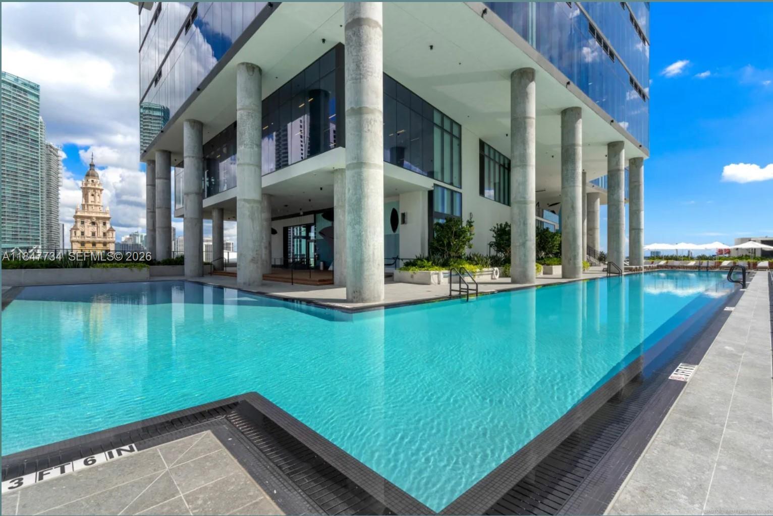 An outdoor swimming pool sits beneath the elevated glass structure of a modern high-rise building — 398 NE 5th St # 4417, Miami FL 33132, MIAMI, FL