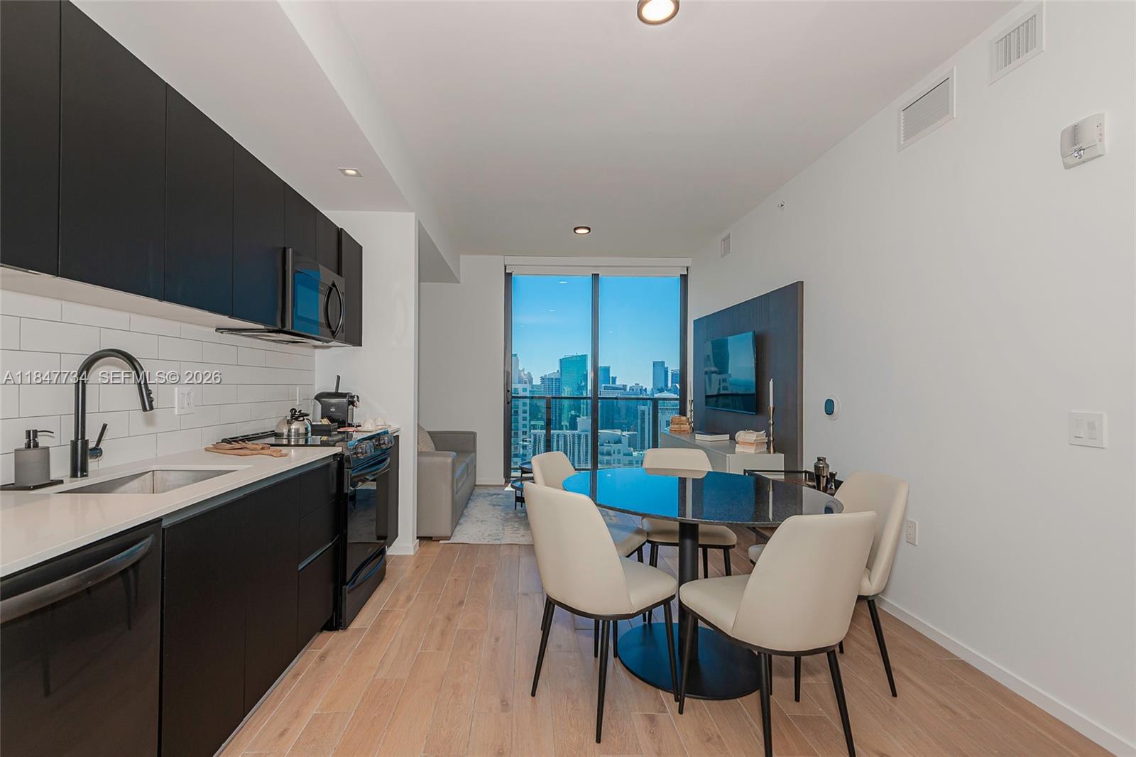 A modern kitchen and dining area features black cabinetry, light wood floors, and city views — 398 NE 5th St # 4417, Miami FL 33132, MIAMI, FL