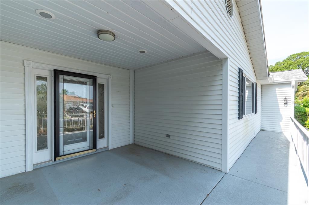 A covered porch with white vinyl siding, a glass storm door, and a concrete floor — 8156 SW 108TH LANE ROAD, OCALA, FL