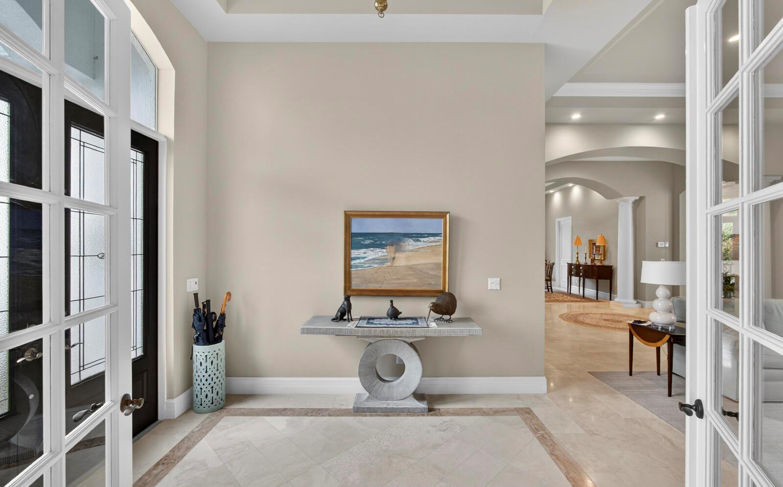 A foyer features a stone console table, a coastal painting, and light-colored tile flooring — 1301 Cape Pointe Circle, Vero Beach FL 32963, VERO BEACH, FL