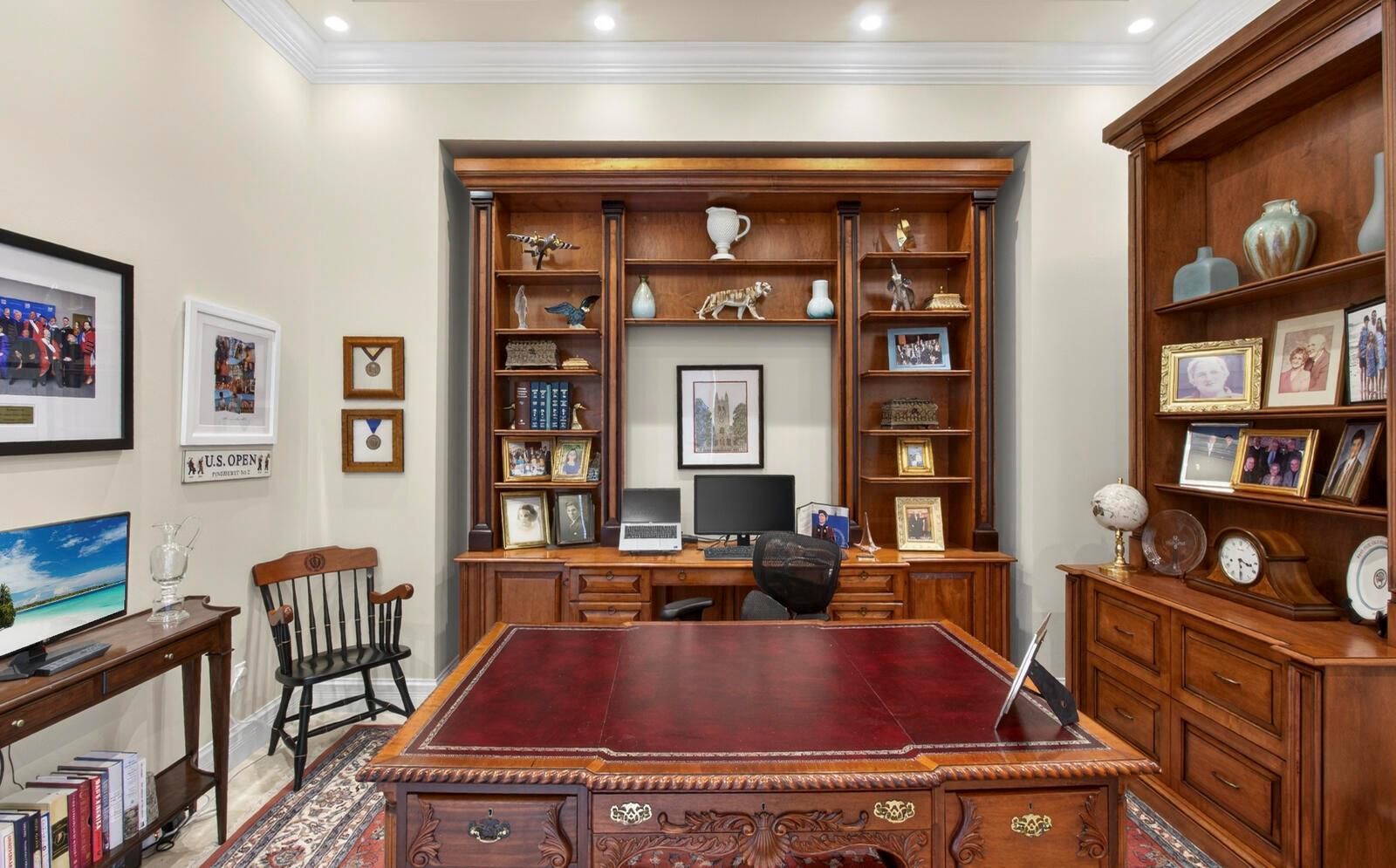 A home office features a large wooden desk, built-in bookshelves, and a patterned area rug — 1301 Cape Pointe Circle, Vero Beach FL 32963, VERO BEACH, FL