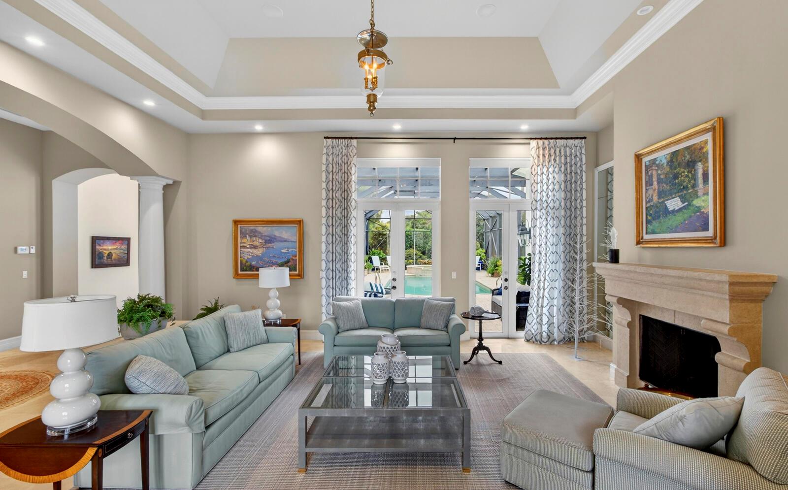 A living room with a tray ceiling, fireplace, and glass doors opening to a pool area — 1301 Cape Pointe Circle, Vero Beach FL 32963, VERO BEACH, FL