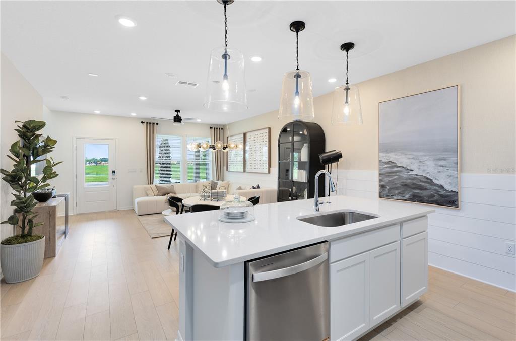 A kitchen island with a stainless steel dishwasher overlooks an open-concept living and dining area — 6258 SUNNY TIME AVENUE, WINTER GARDEN, FL