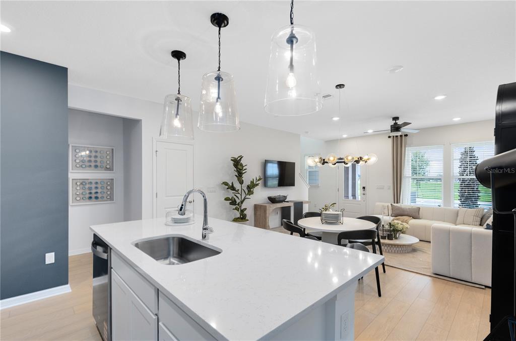 A modern kitchen island with a sink overlooks an open-concept dining and living area — 6258 SUNNY TIME AVENUE, WINTER GARDEN, FL