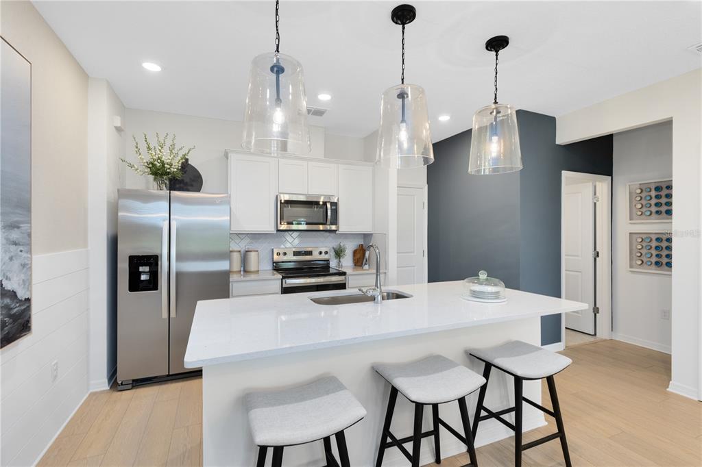 A modern kitchen features white cabinetry, stainless steel appliances, a quartz island, and three barstools — 6258 SUNNY TIME AVENUE, WINTER GARDEN, FL