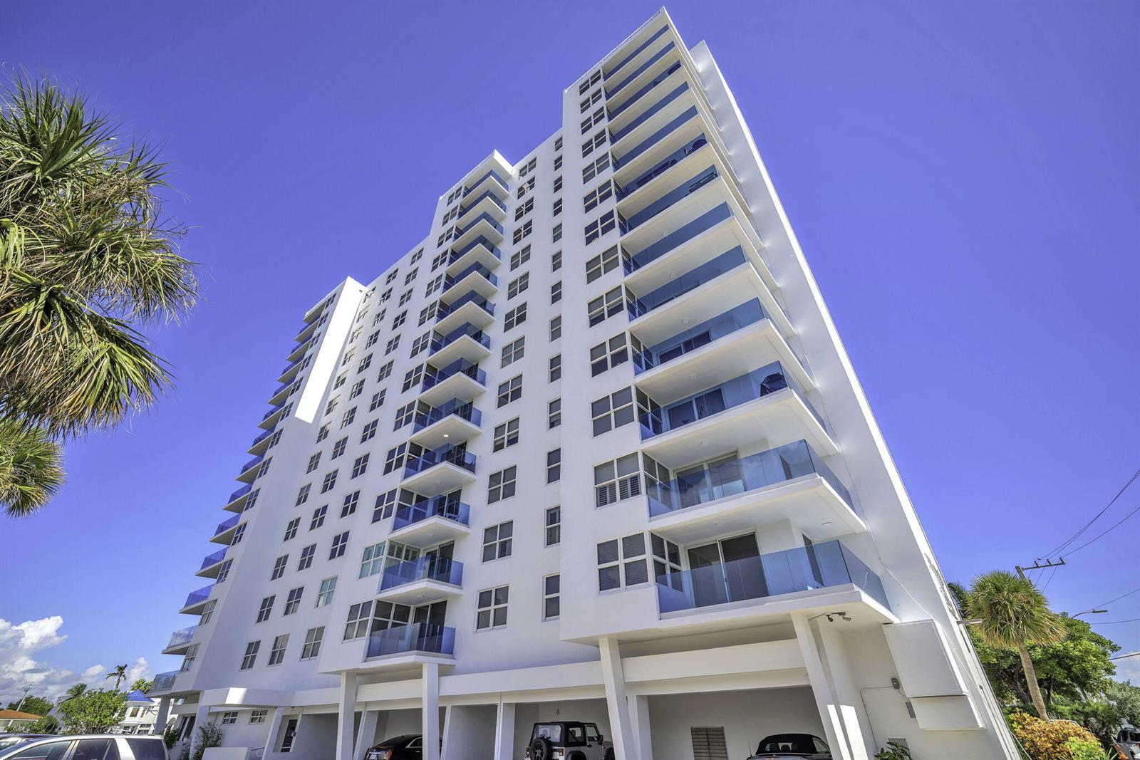 A tall white residential building features stacked balconies with glass railings and a ground-level parking area — 2639 N Riverside Drive # 505, Pompano Beach FL 33062, POMPANO BEACH, FL
