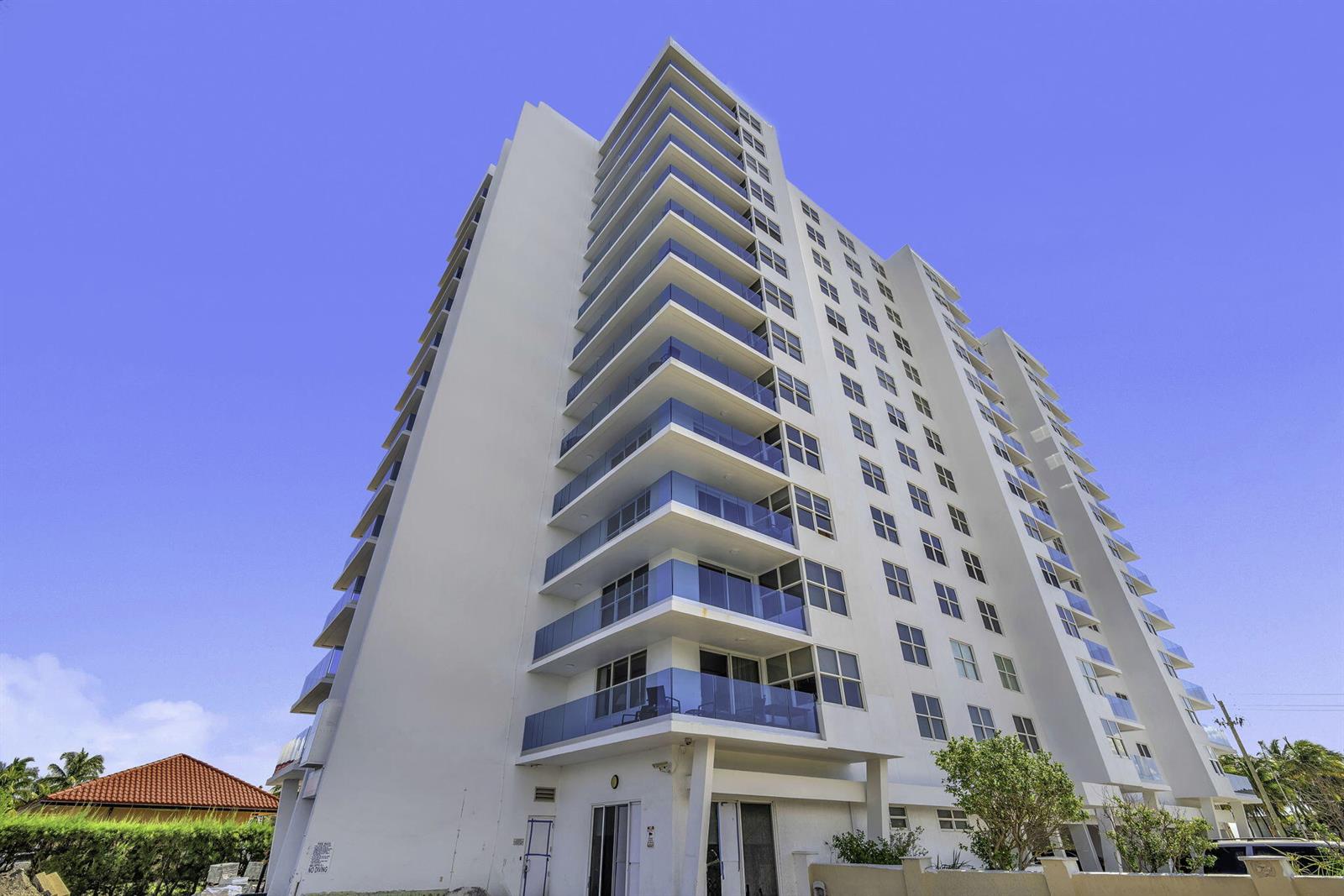 A low-angle view of a tall white residential building with stacked glass-railed balconies — 2639 N Riverside Drive # 505, Pompano Beach FL 33062, POMPANO BEACH, FL