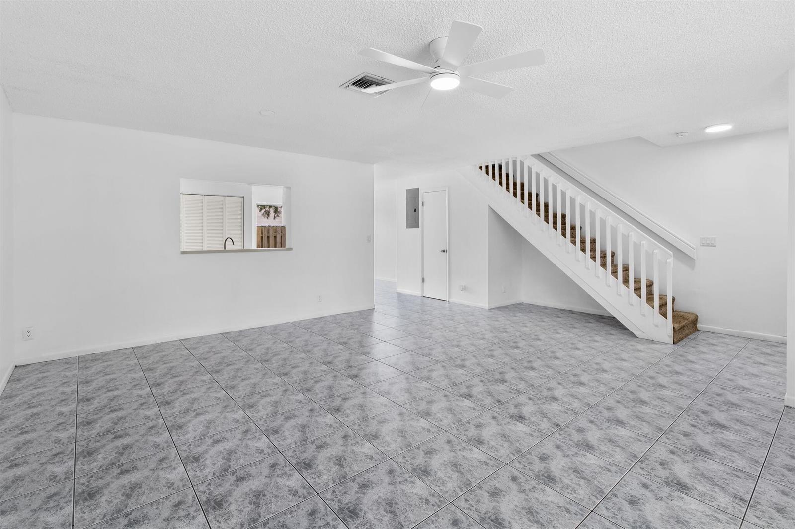 An empty living room features gray tile flooring, a white staircase, and a ceiling fan — 12212 NW 36th Place, Sunrise FL 33323, SUNRISE, FL