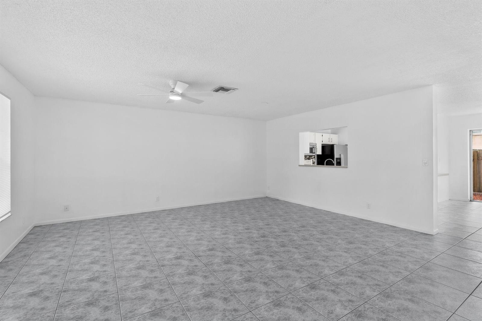 An empty living room with gray tiled floors, white walls, and a ceiling fan — 12212 NW 36th Place, Sunrise FL 33323, SUNRISE, FL