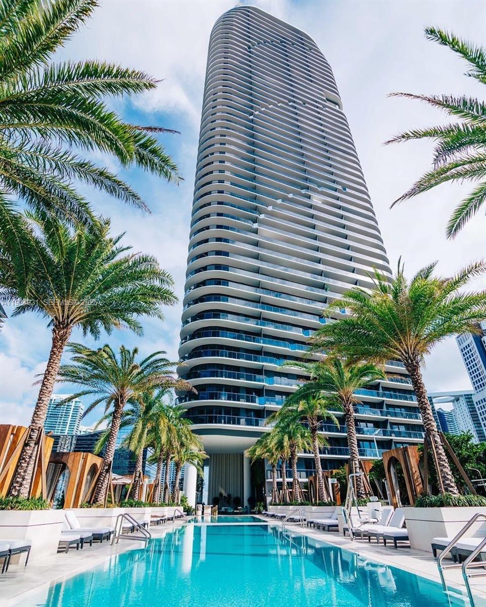 A tall, modern residential skyscraper rises above a swimming pool surrounded by palm trees — 801 S Miami Ave # 509, Miami FL 33130, MIAMI, FL