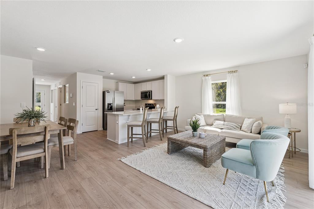 An open-concept living room and kitchen featuring light wood flooring and white cabinetry — 1651 GREAT OSPREY WAY, NEW SMYRNA BEACH, FL
