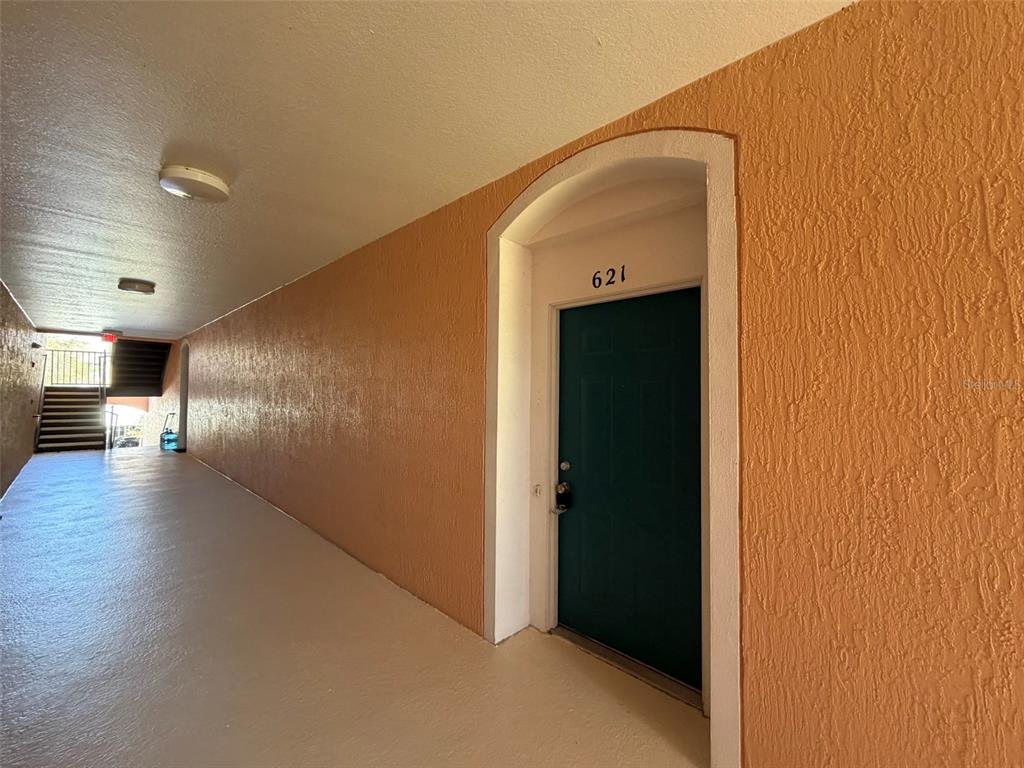 An outdoor apartment hallway features a dark green door labeled 621 and orange textured walls — 13524 TURTLE MARSH LOOP UNIT 621, ORLANDO, FL