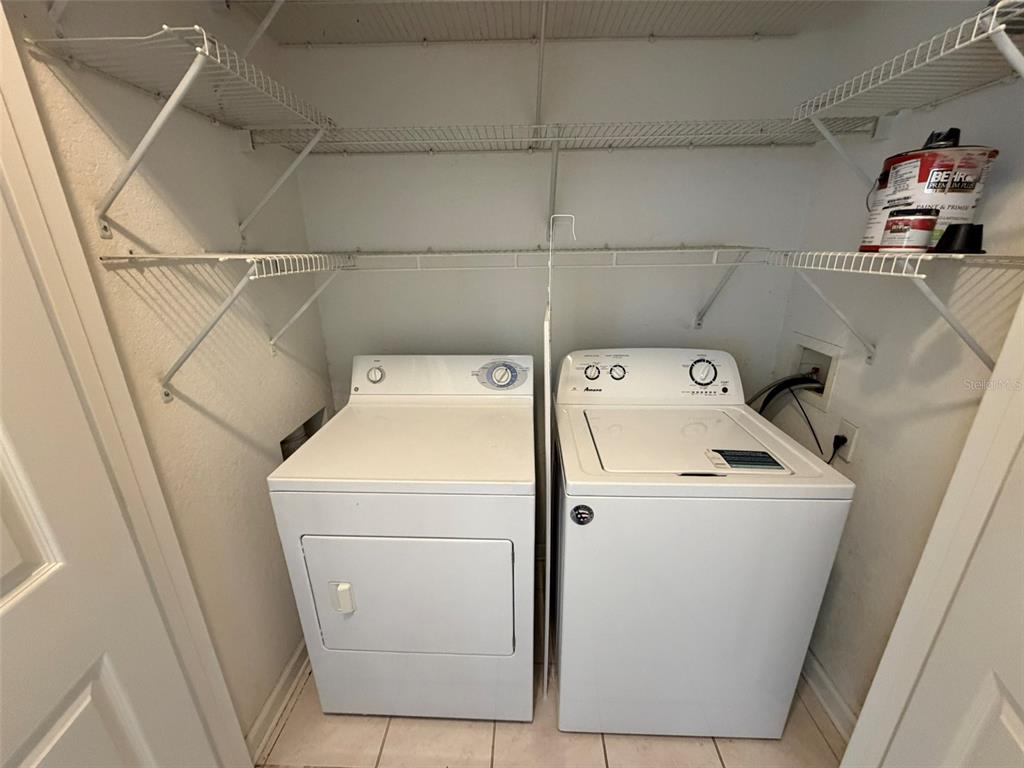 A laundry closet contains a white washer and dryer beneath wire shelving — 13524 TURTLE MARSH LOOP UNIT 621, ORLANDO, FL