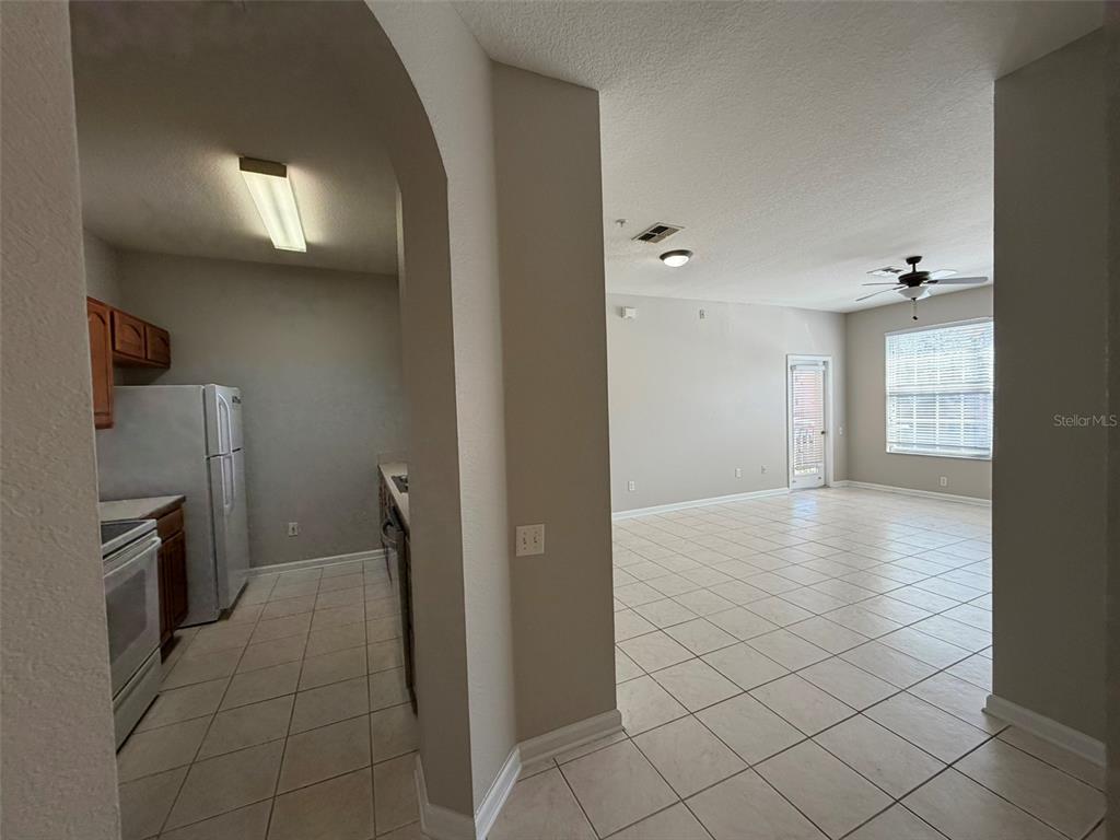 A kitchen with white appliances and wood cabinets opens into a large tiled living area — 13524 TURTLE MARSH LOOP UNIT 621, ORLANDO, FL