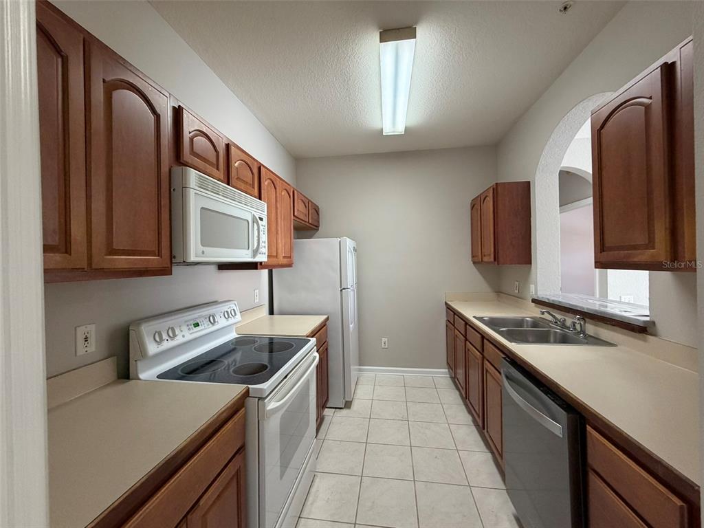 A galley-style kitchen features wood cabinets, white appliances, a double sink, and tile flooring — 13524 TURTLE MARSH LOOP UNIT 621, ORLANDO, FL