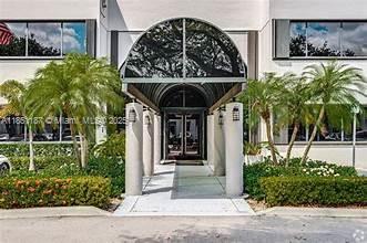 The exterior entrance of a commercial building features a curved metal awning and palm trees — 14261 Commerce Way # 200, Miami Lakes FL 33016, MIAMI LAKES, FL