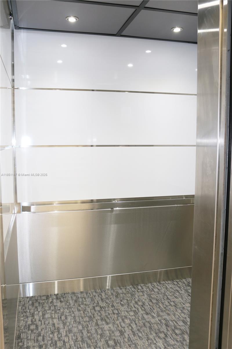 The interior of an elevator features white panels, stainless steel accents, and gray carpeted flooring — 14261 Commerce Way # 200, Miami Lakes FL 33016, MIAMI LAKES, FL