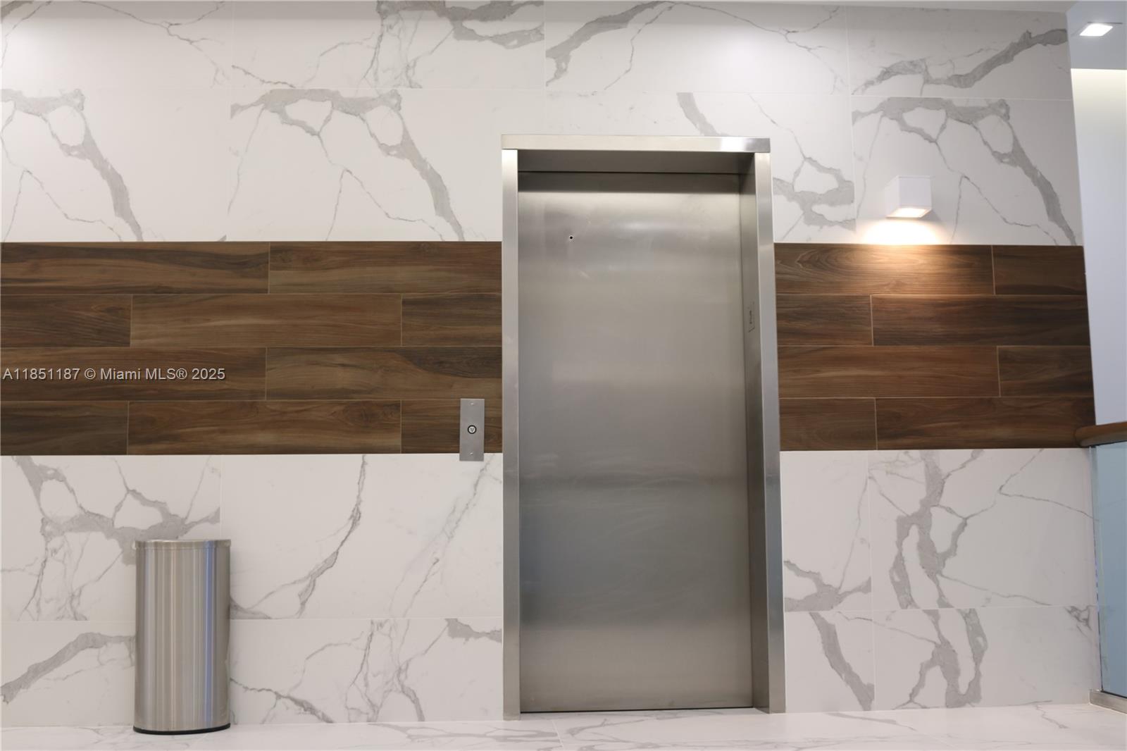 An elevator door is centered on a wall with marble tile and wood-look panels — 14261 Commerce Way # 200, Miami Lakes FL 33016, MIAMI LAKES, FL