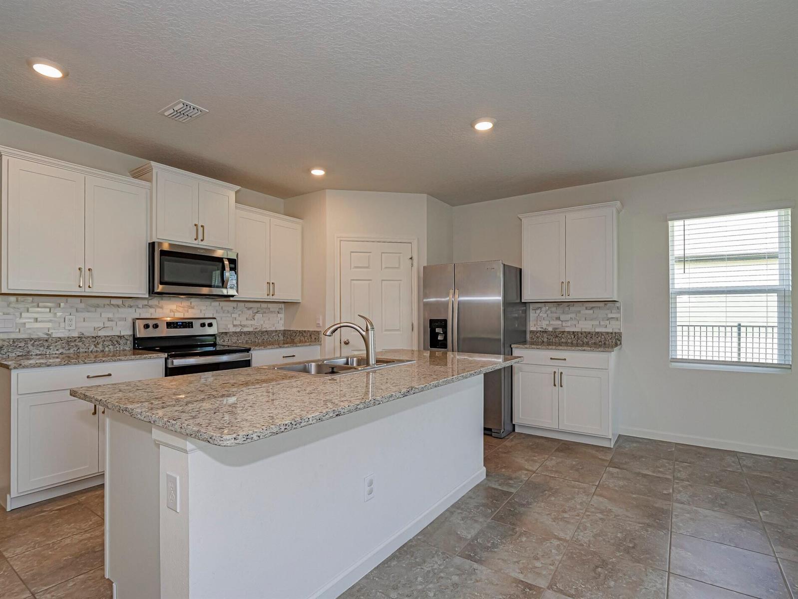 A kitchen features white cabinets, granite countertops, stainless steel appliances, and a central island — 4103 Keeson Circle, Vero Beach FL 32967, VERO BEACH, FL