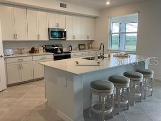 A modern kitchen features white cabinets, a large island with bar stools, and stainless appliances — 17665 BORACAY COURT UNIT 101, VENICE, FL