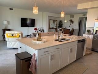 A kitchen island with a sink and white cabinets overlooks a living room and dining area — 17665 BORACAY COURT UNIT 101, VENICE, FL