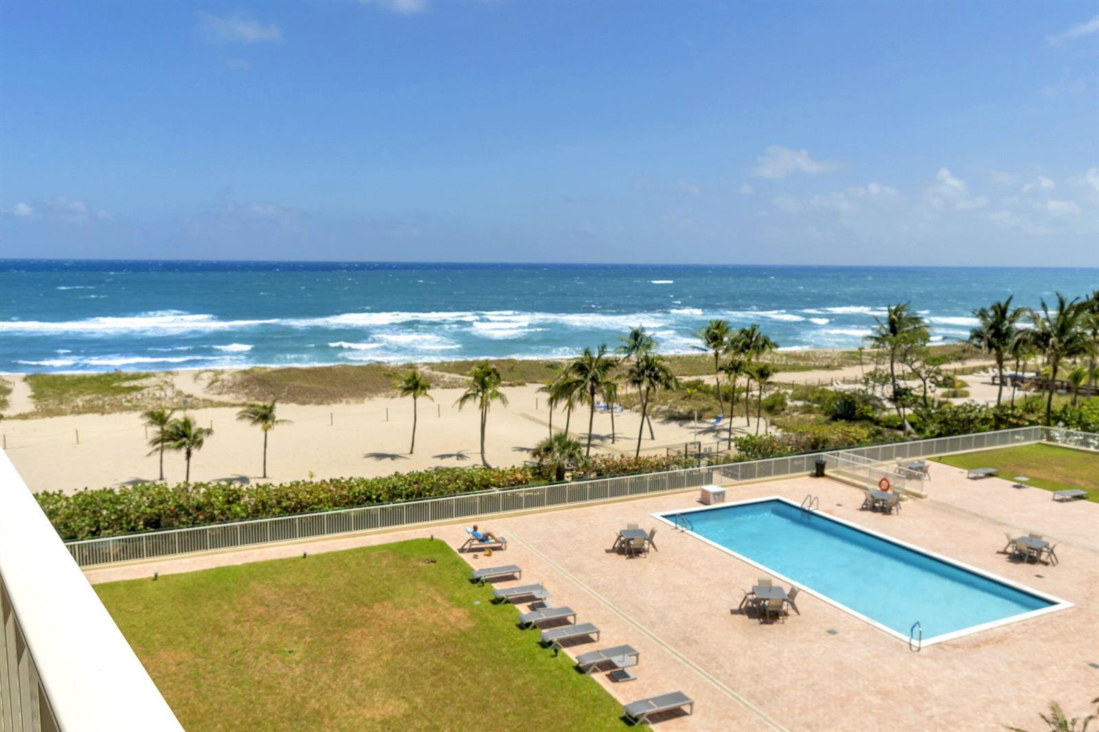 An elevated view of a swimming pool, lawn, and sandy beach overlooking the ocean — 750 N Ocean Boulevard Apt 604, Pompano Beach FL 33062, POMPANO BEACH, FL