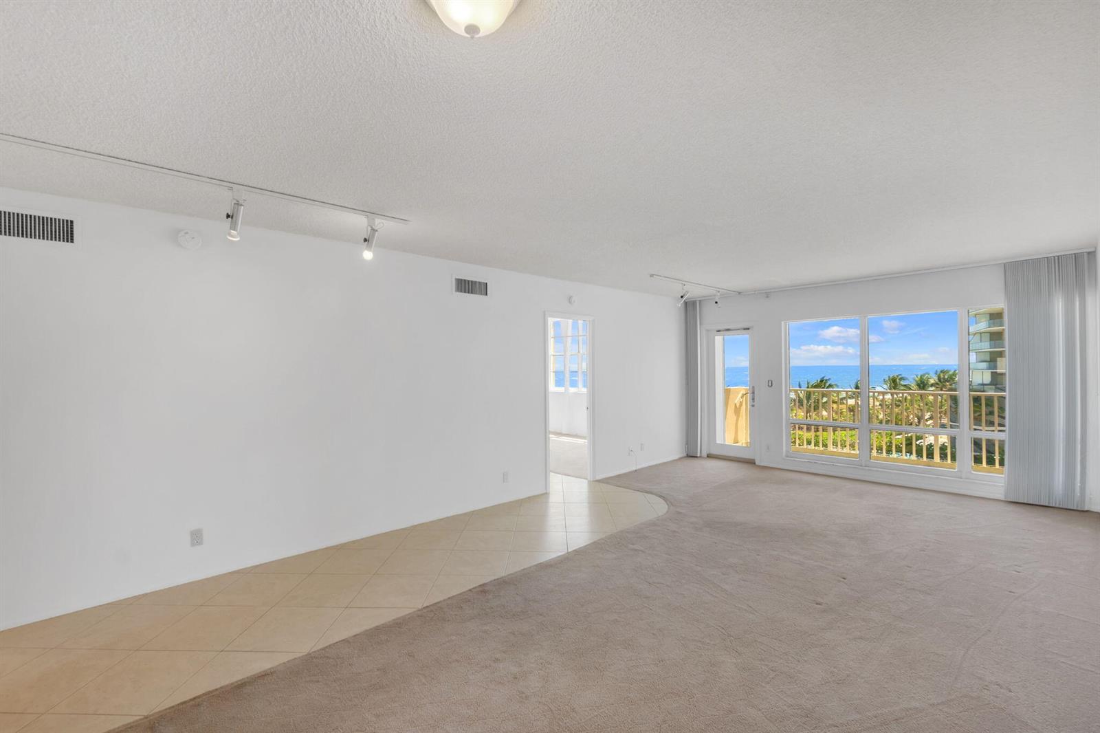 An empty living room features beige carpet, tiled flooring, track lighting, and a balcony view — 750 N Ocean Boulevard Apt 604, Pompano Beach FL 33062, POMPANO BEACH, FL