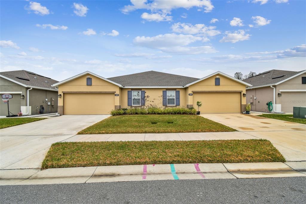A single-story duplex with two garages, tan stucco siding, and a central lawn — 18053 TURNING LEAF CIRCLE, LAND O LAKES, FL