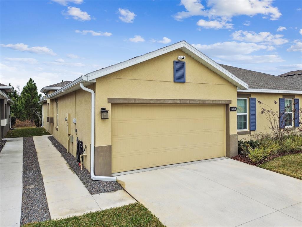 A yellow stucco house features a two-car garage and a concrete driveway with gravel strips — 18053 TURNING LEAF CIRCLE, LAND O LAKES, FL