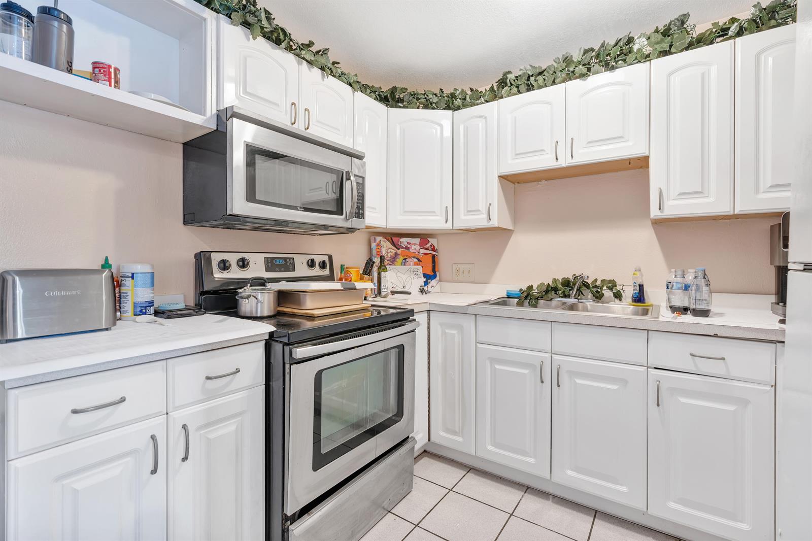 A white kitchen features white cabinets, a black stove, a microwave, and tile flooring — 505 Foresteria Drive, Lake Park FL 33403, LAKE PARK, FL