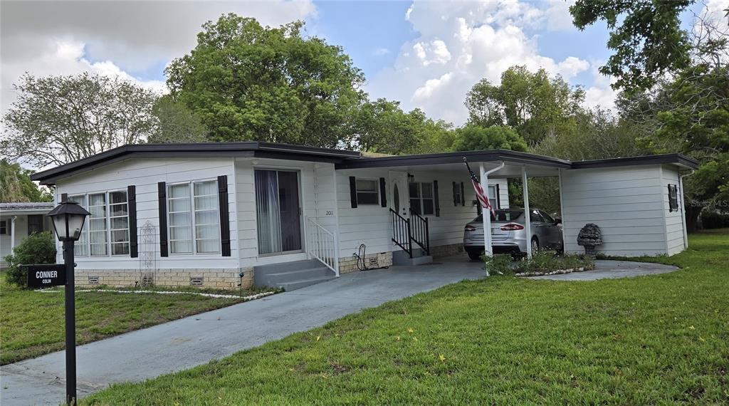 A white single-story manufactured home features a carport, a concrete driveway, and a front lawn — 2011 OAK GROVE DRIVE UNIT 39, ZELLWOOD, FL