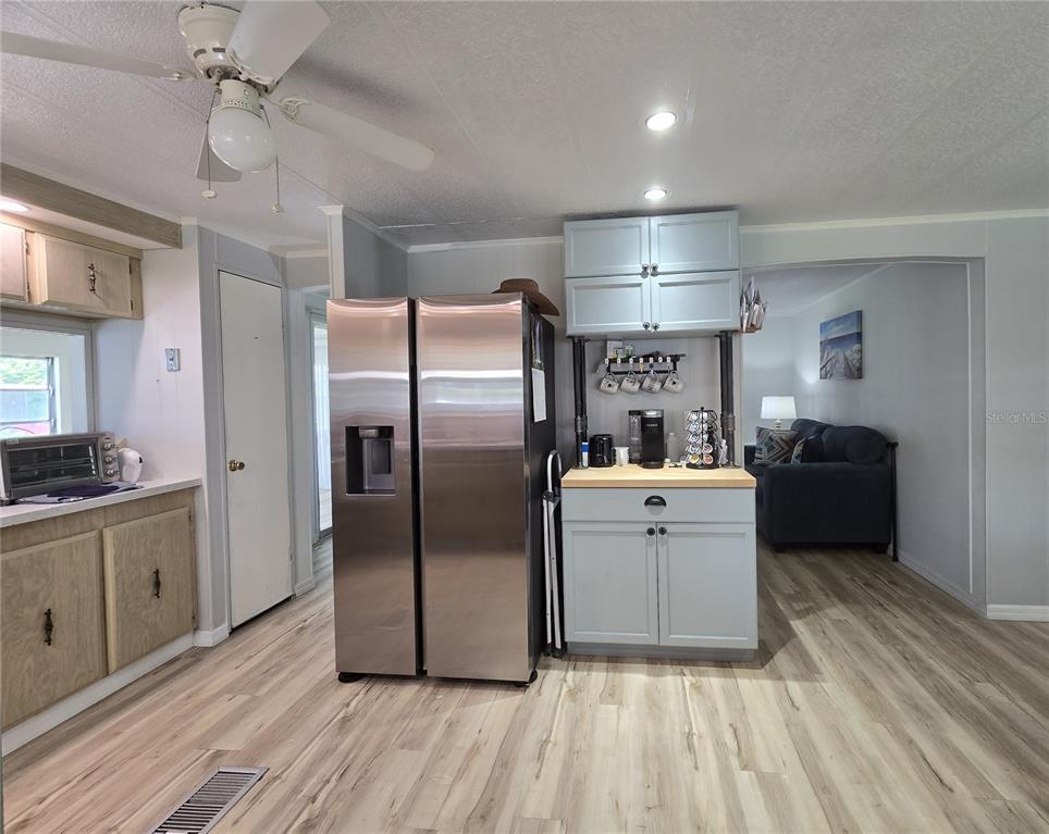 A kitchen features light wood-look flooring, a stainless steel refrigerator, and a blue coffee station — 2011 OAK GROVE DRIVE UNIT 39, ZELLWOOD, FL