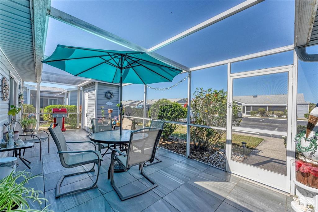 A screened-in patio features tiled flooring, a dining set with a teal umbrella, and landscaping — 3300 LOVELAND BOULEVARD UNIT 1201, PUNTA GORDA, FL