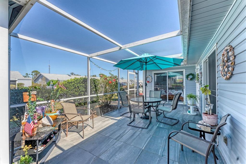 A screened-in patio features gray tile flooring, a dining set with a blue umbrella, and chairs — 3300 LOVELAND BOULEVARD UNIT 1201, PUNTA GORDA, FL