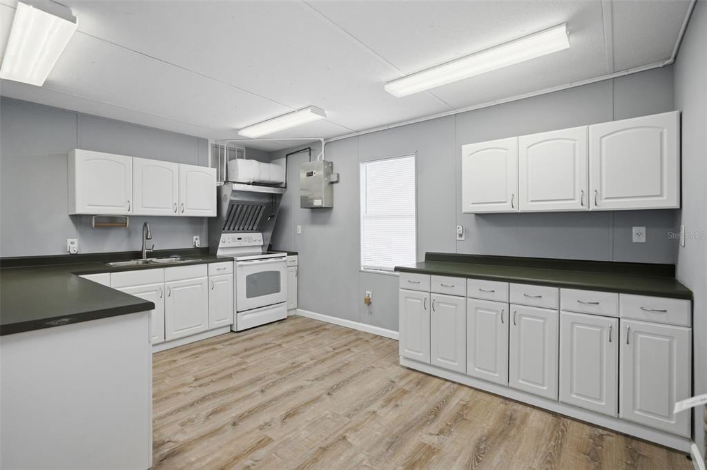 A kitchen with white cabinets, dark countertops, light wood-look flooring, and fluorescent lighting — 15464 CORTEZ BOULEVARD, BROOKSVILLE, FL