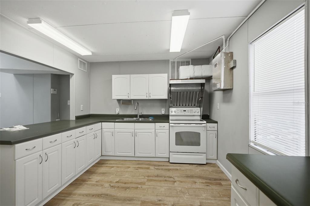 A kitchen features white cabinetry, dark countertops, a white stove, and light wood-look flooring — 15464 CORTEZ BOULEVARD, BROOKSVILLE, FL