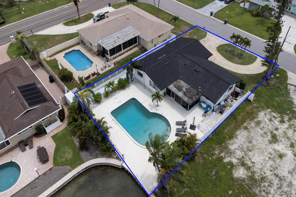 An aerial view shows a house with a black roof, a pool, and a canal — 12125 6TH STREET E, TREASURE ISLAND, FL